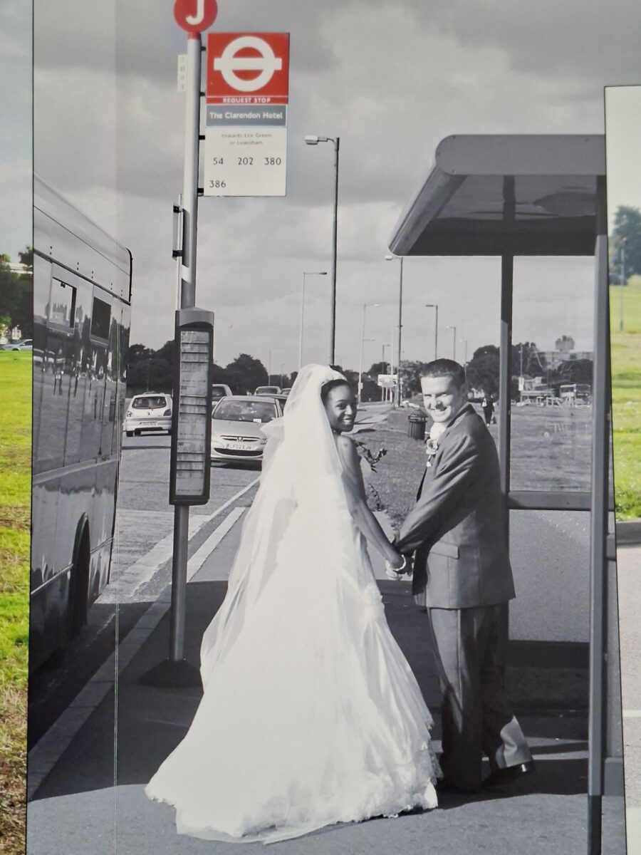Tania and James holding hands at a London bus stop near The Clarendon Hotel, Tania wearing her Sophia Tolli strapless lace gown and veil.