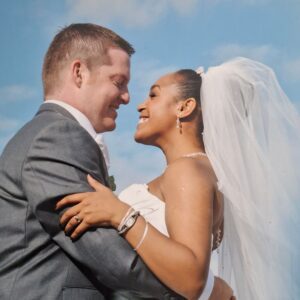 Tania in her strapless Sophia Tolli lace bridal gown smiling up at James beneath a blue sky at their autumn wedding.