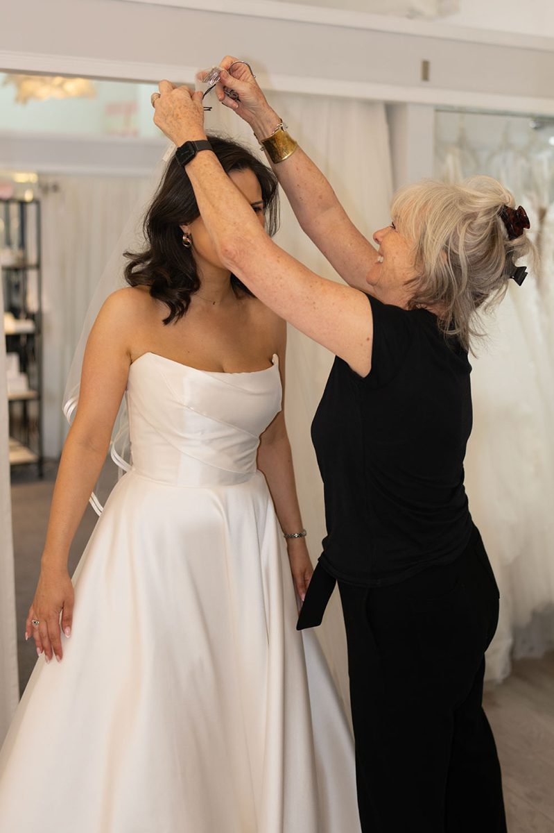 A stylist places a veil on a bride in the boutique