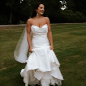 Sophie in her strapless satin Maggie Sottero mermaid gown and veil, smiling as she walks across the grounds at Cluny Castle.