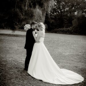 Sarah in her strapless Mori Lee corset gown with a long train, touching foreheads with Anthony in a romantic outdoor portrait.