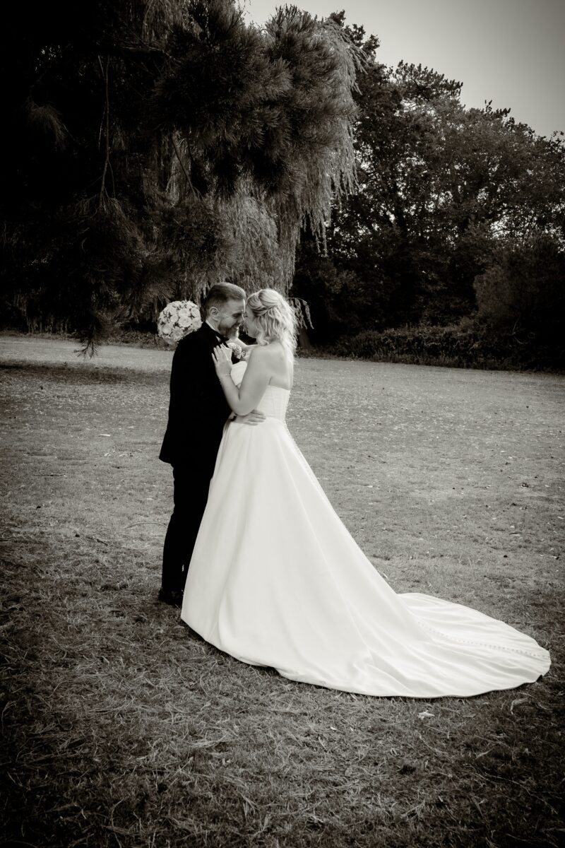 Sarah in her strapless Mori Lee corset gown with a long train, touching foreheads with Anthony in a romantic outdoor portrait.