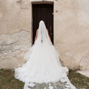 The back of Bella's Justin Alexander tiered waterfall gown and lace-trimmed cathedral veil, in front of an old wooden door.