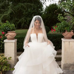 Bella in her Justin Alexander tiered waterfall tulle ballgown and veil, smiling on garden steps in Italy.