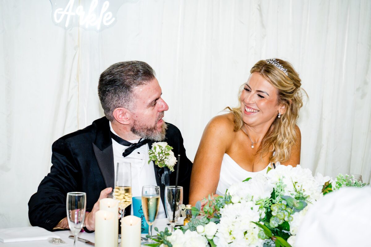 Sarah in her strapless corset Mori Lee gown laughing with Anthony at the top table during their wedding reception at The Manor at Bickley.