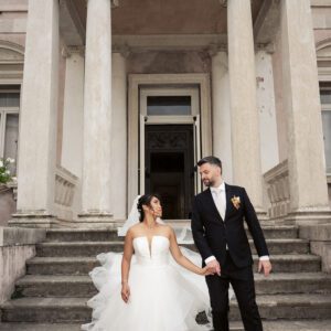 Bella in her strapless Justin Alexander tiered waterfall gown holding hands with Alessandro on wide stone steps in Italy.