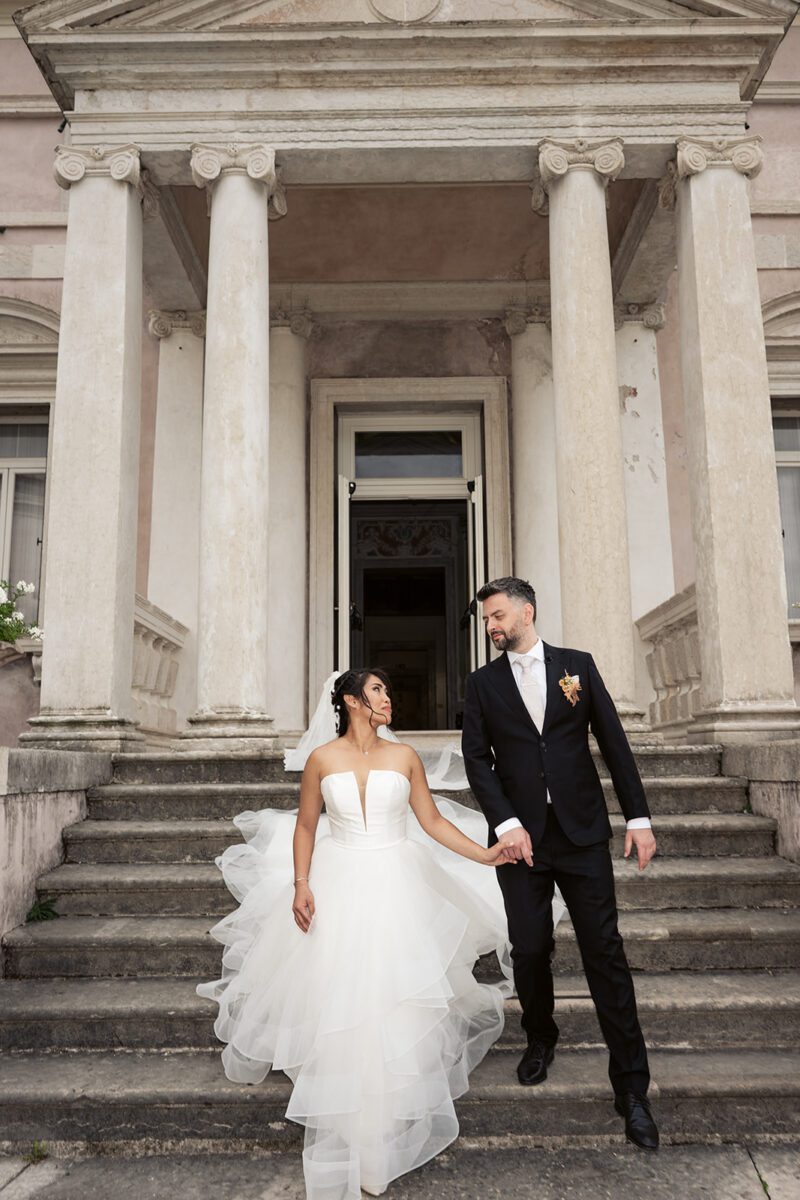 Bella in her strapless Justin Alexander tiered waterfall gown holding hands with Alessandro on wide stone steps in Italy.