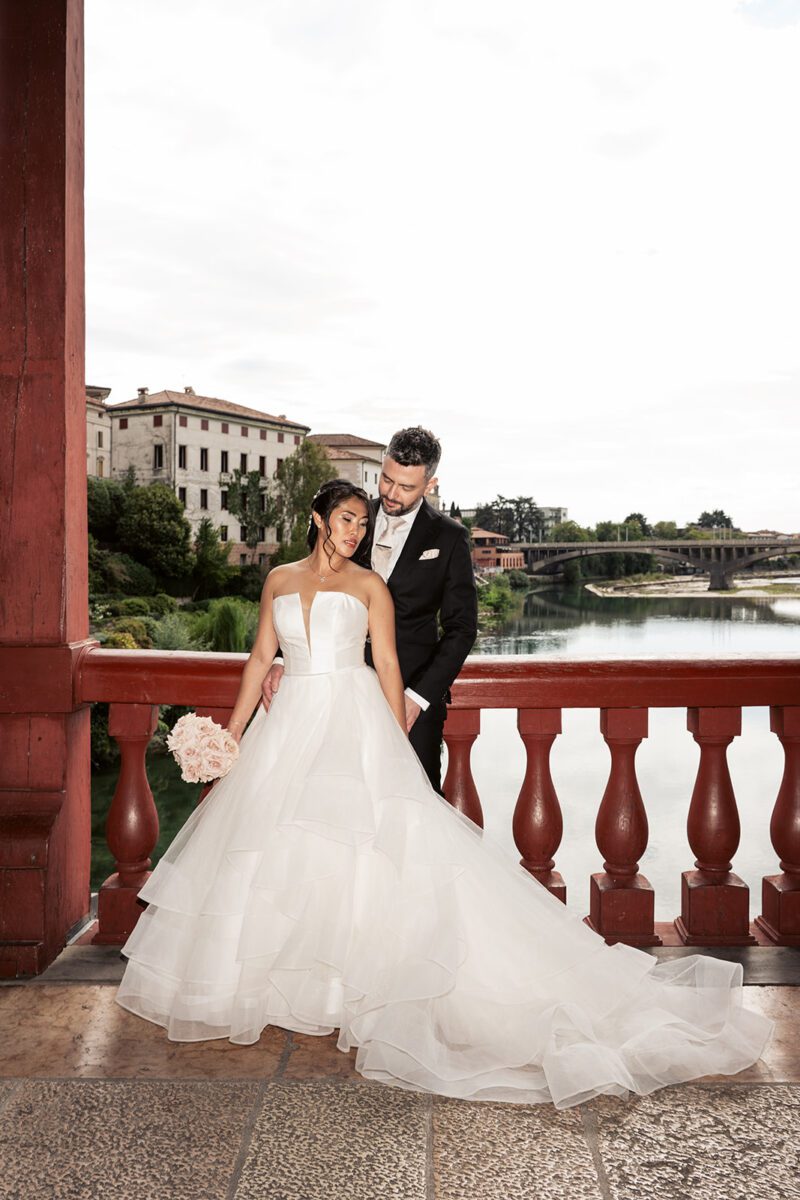 Bella in her Justin Alexander tiered waterfall gown with Alessandro on the red balustrade of the Ponte Vecchio, Bassano del Grappa.