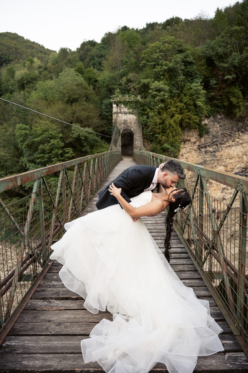 Alessandro dipping Bella for a kiss on the suspension bridge over Lago del Corlo, her Justin Alexander tiered gown spread out behind her.