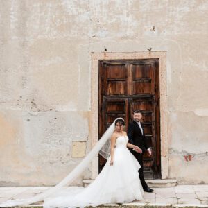 Bella in her Justin Alexander tiered waterfall gown with Alessandro by an old stone doorway in Italy.