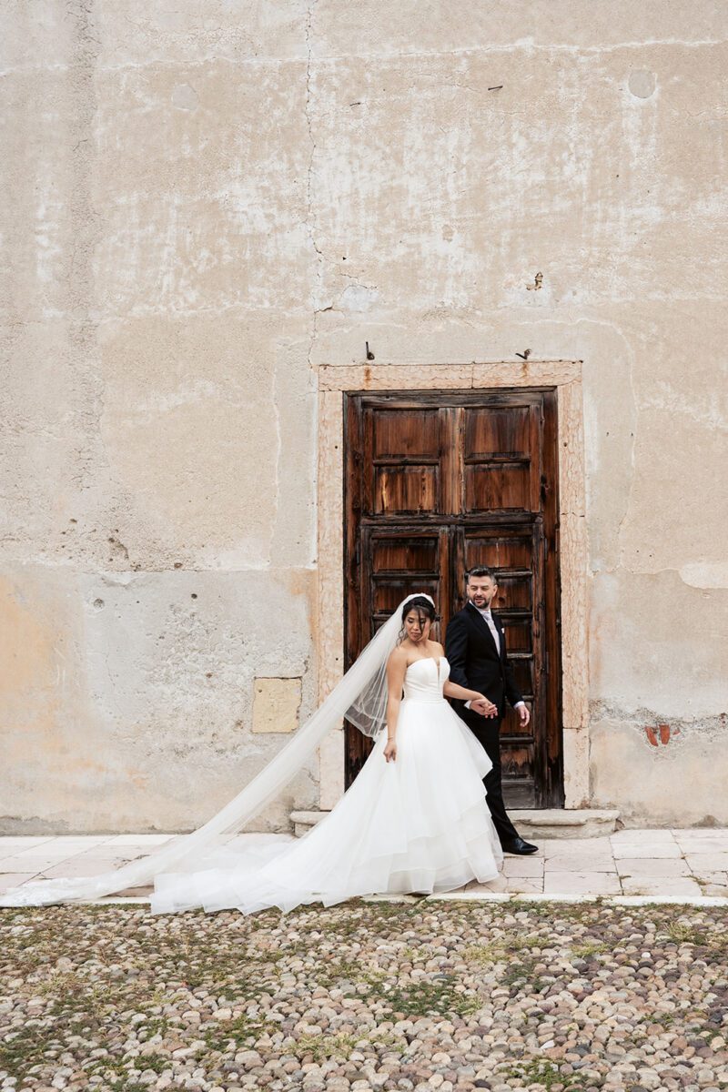 Bella in her Justin Alexander tiered waterfall gown with Alessandro by an old stone doorway in Italy.