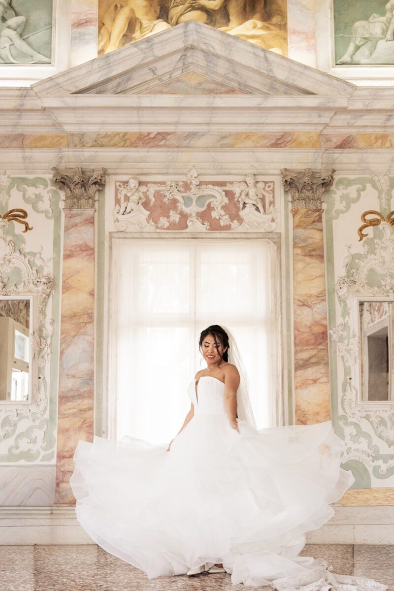 Bella twirling in her Justin Alexander tiered waterfall gown and veil inside the ornate marble halls of Palazzo Sturm, Italy.